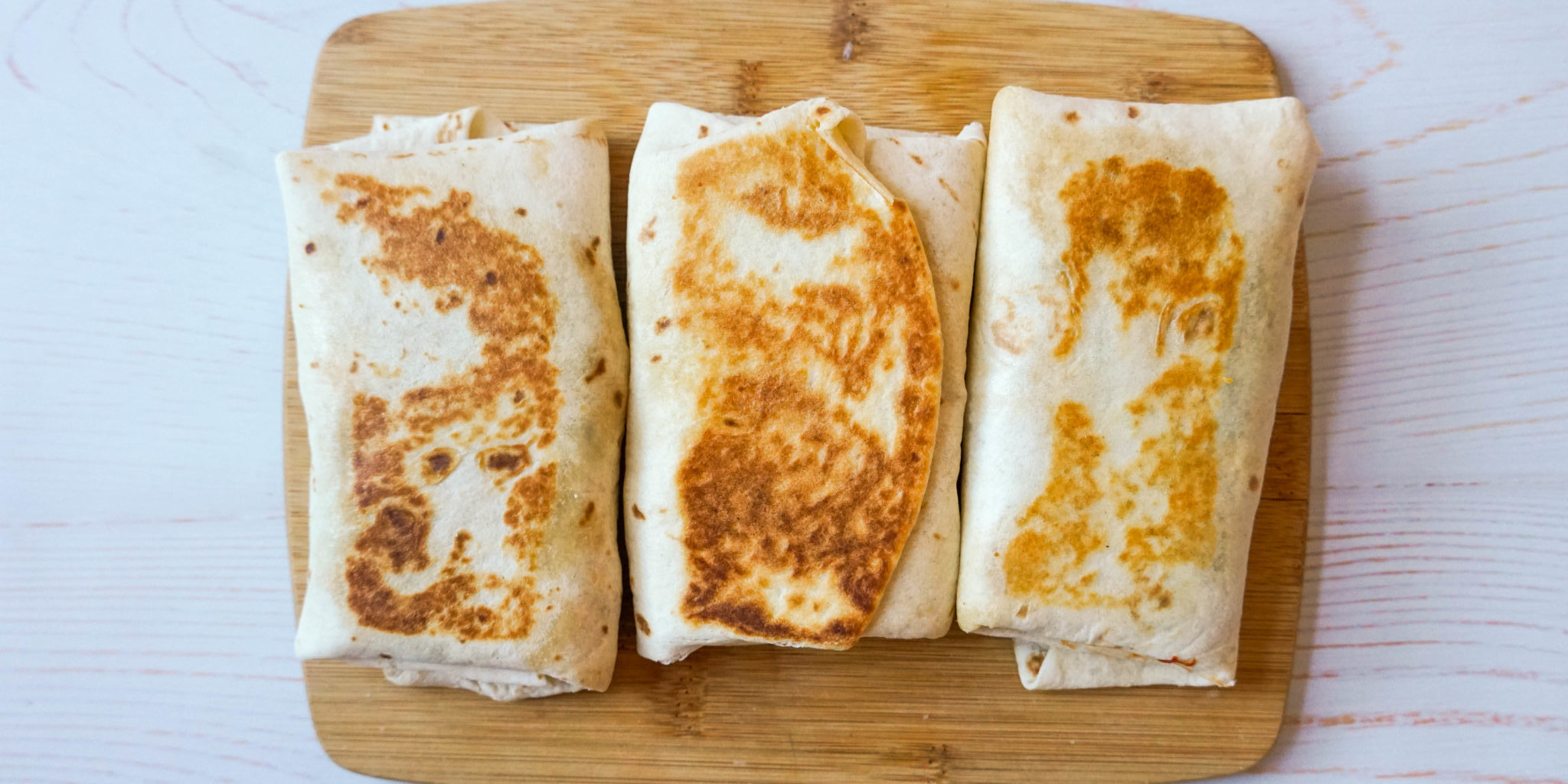 Three golden breakfast starbucks copycat recipe wraps are placed side by side on top of a brown wooden cutting board.