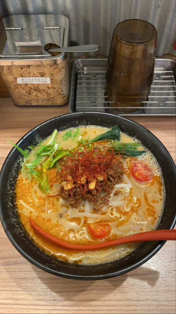 Bowl of ramen noodles with decorative garnish on top and an orange spoon.