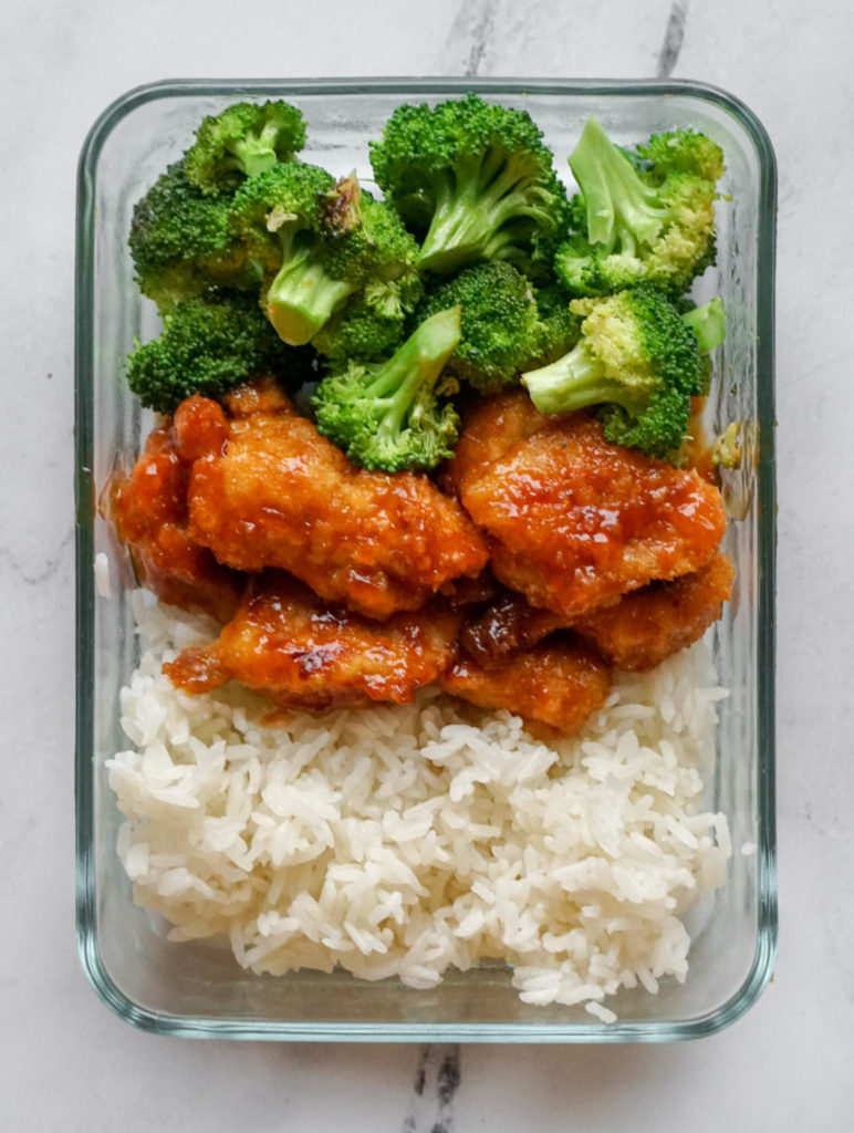 A rectangular glass container that has broccoli, orange chicken, and white rice