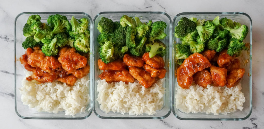 Three glass rectangular containers that have broccoli, orange chicken, and white rice.