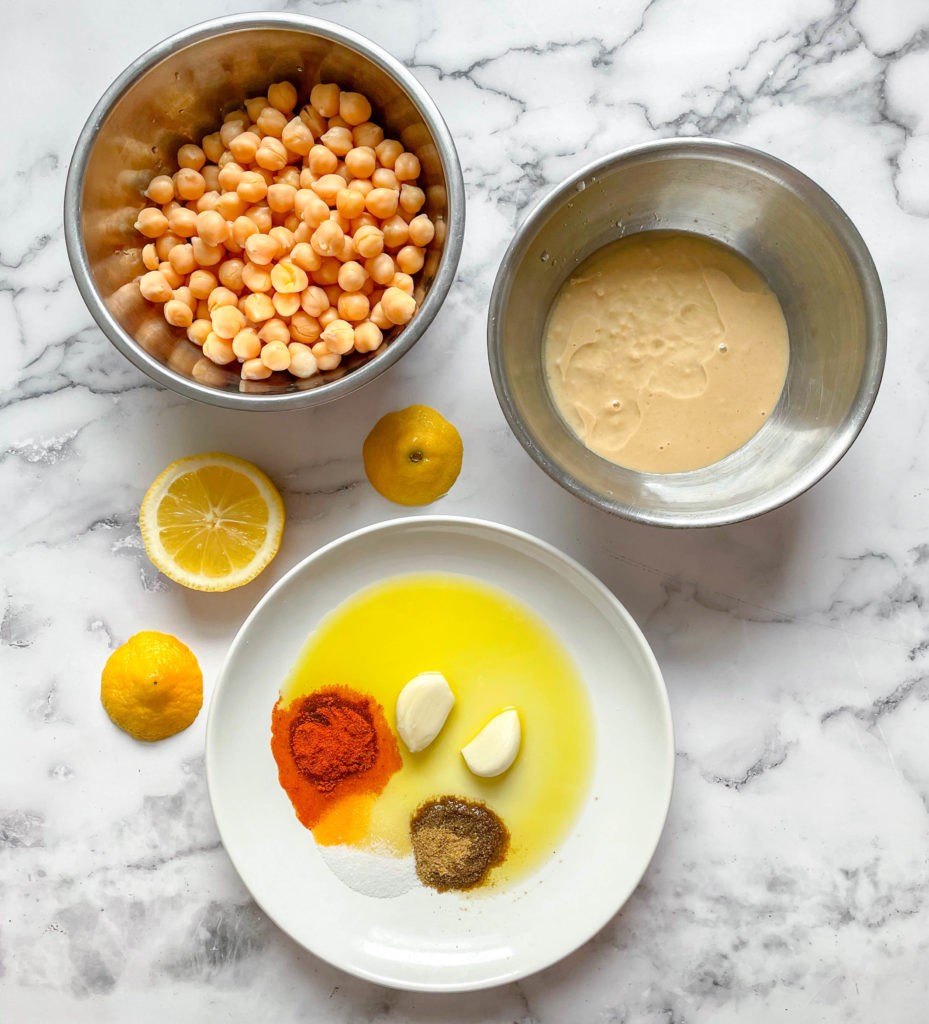 Ingredients used to make homemade hummus. Including chickpeas, tahini, lemons, garlic, oil, and spices.