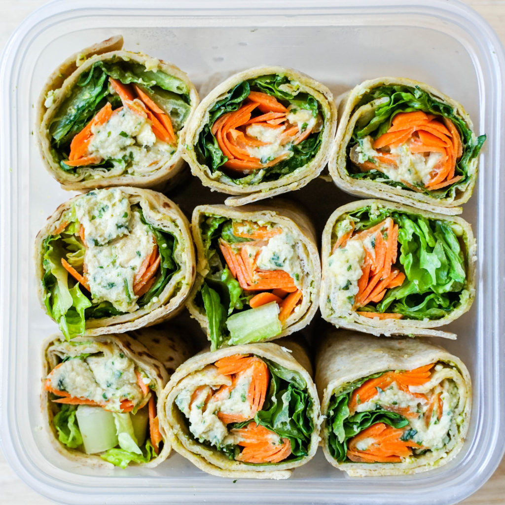Nine small open wraps with colorful veggies in a square plastic container.