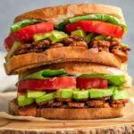 Two BLT sandwiches are stacked on top of each other on a wood cutting board