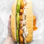 A long bread roll is on its side filled with buffalo tempeh, avocado, and coleslaw