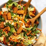A bowl with wooden spoon sticking out. The bowl contains a colorful green and orange salad