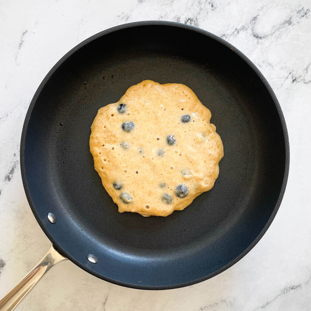 a blueberry lemon pancake cooking on a nonstick pan