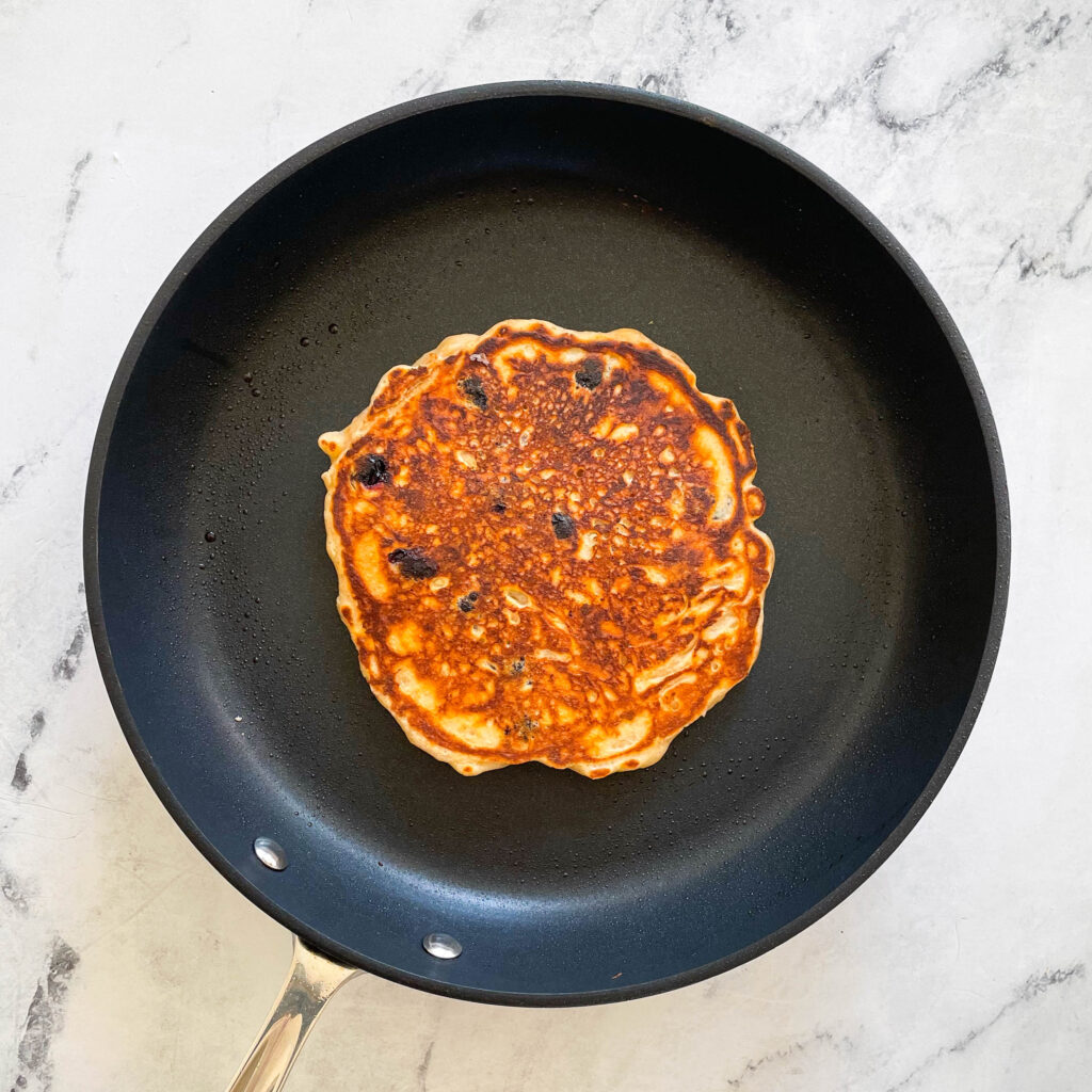 a perfectly cooked blueberry lemon pancake on a black nonstick pan