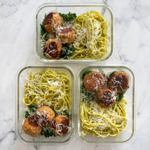 3 containers with meatballs and spagehtti in a green sauce, covered in parmesan cheese.