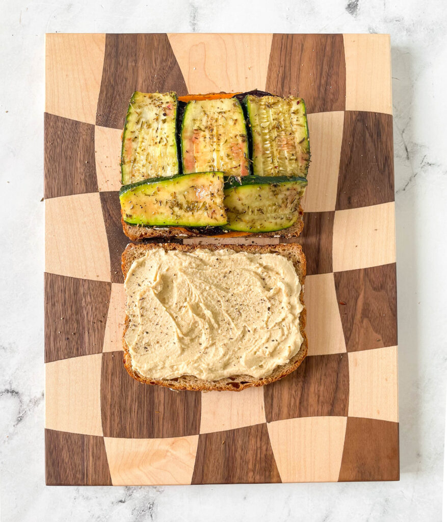 two pieces of bread, one with roasted zucchini and one with hummus spread